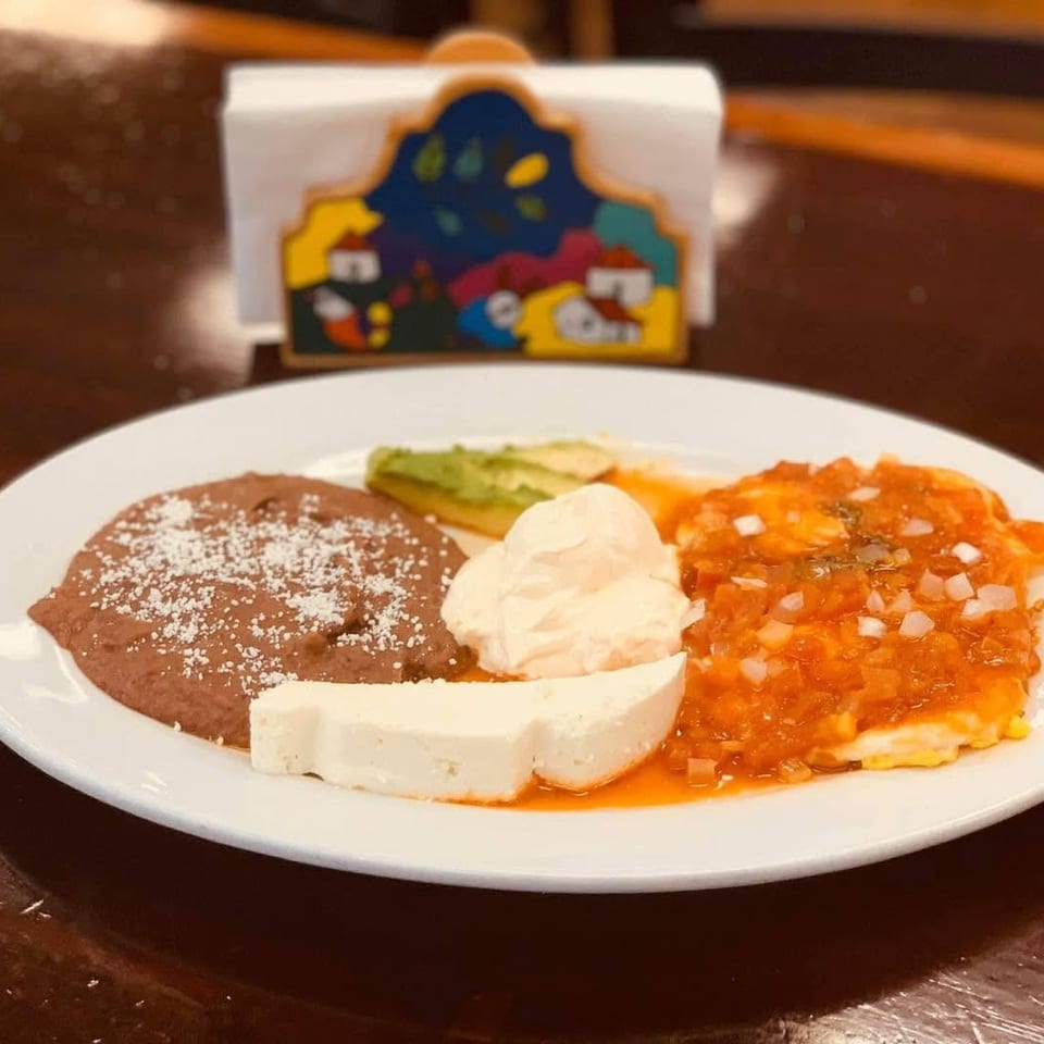 Mexican-style platter with refried beans, red-sauced enchiladas, avocado, white cheese, and sour cream on a restaurant table.
