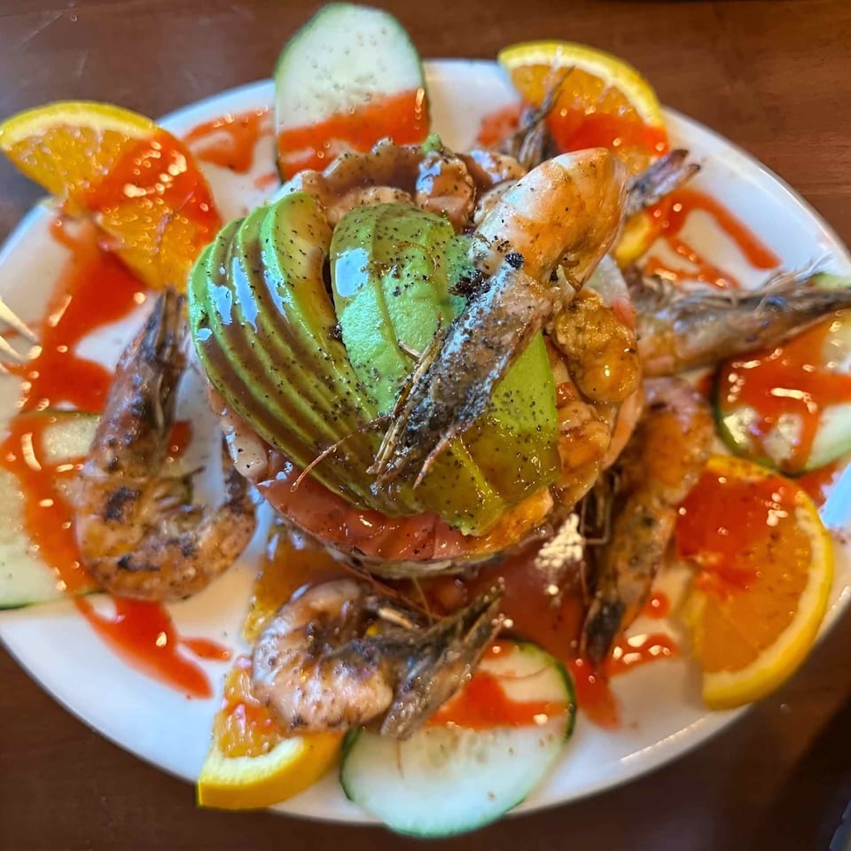 Seafood platter with shrimp, mussels, avocado, cucumber, tomato, and citrus wedges drizzled with red sauce.