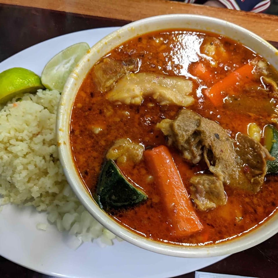Bowl of red curry with chicken and vegetables served alongside white rice and lime wedges.