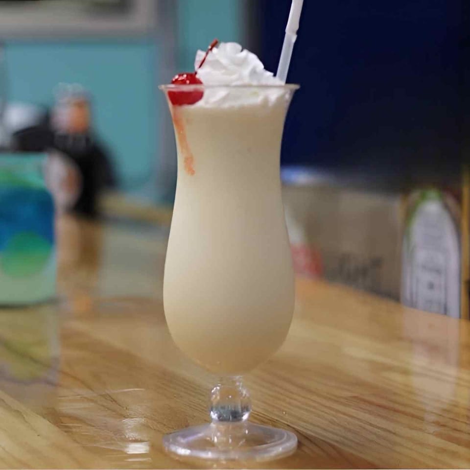 Creamy milkshake topped with whipped cream, cherries, and a straw on a wooden restaurant table.