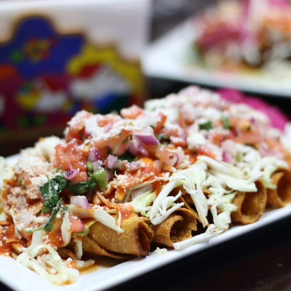 Loaded tortilla chips topped with shredded cabbage, diced tomatoes, onions, cilantro, salsa, and crumbled cheese on a white plate.