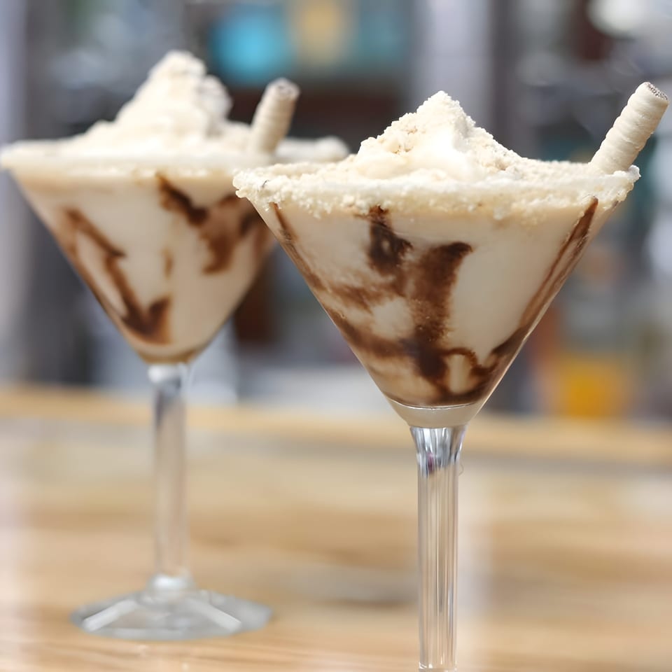Two creamy chocolate-swirled desserts in martini glasses, topped with whipped cream and wafer sticks on a restaurant table.
